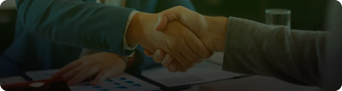 Two people shaking hands over documents at a desk